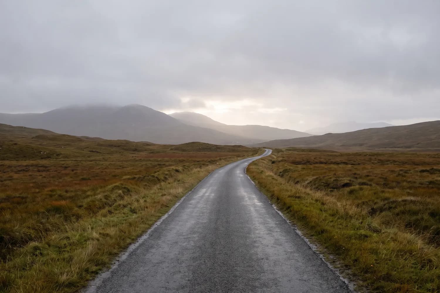 A damp single-track road running into soft grey rain-light with low cloud sitting on the hills
